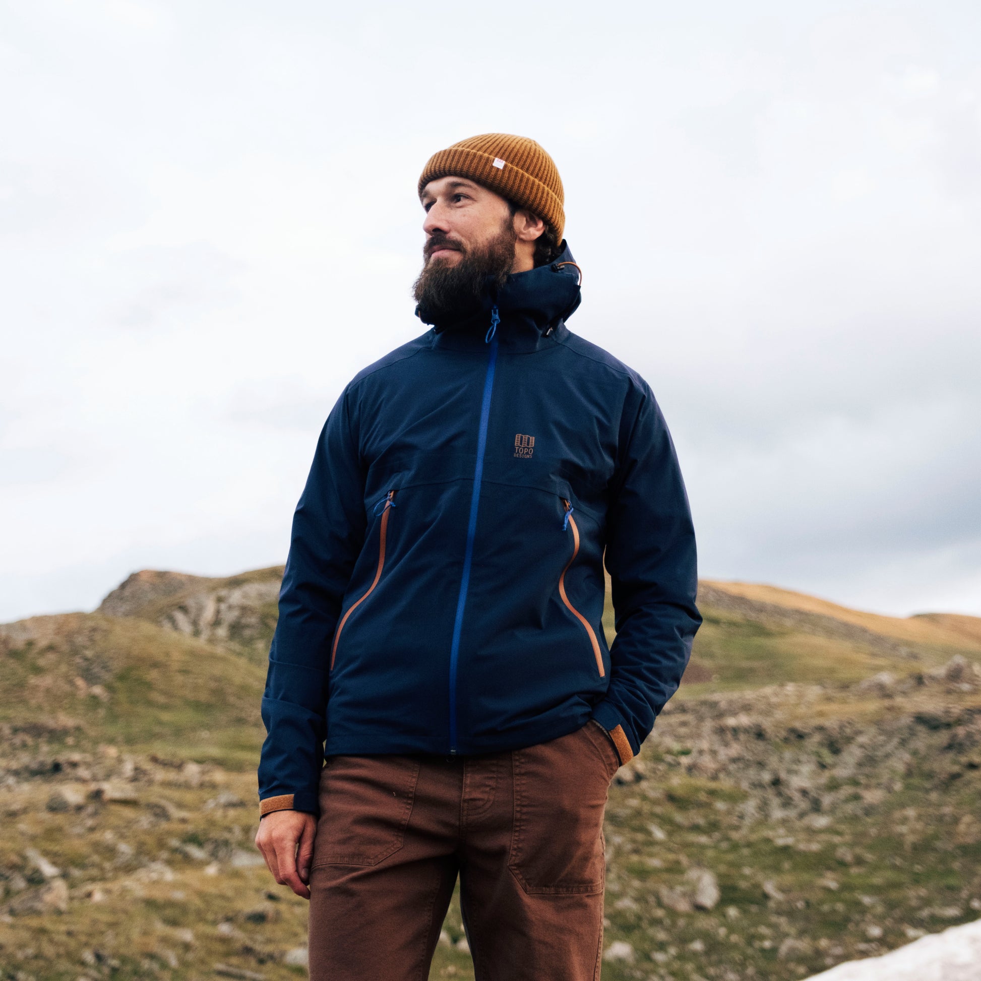 General Image of a man wearing a blue global jacket and brown beanie standing in a mountainous landscape